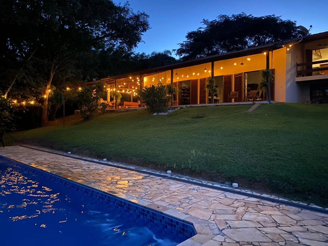Sítio Manacás iluminado ao entardecer com varal de luzes e piscina