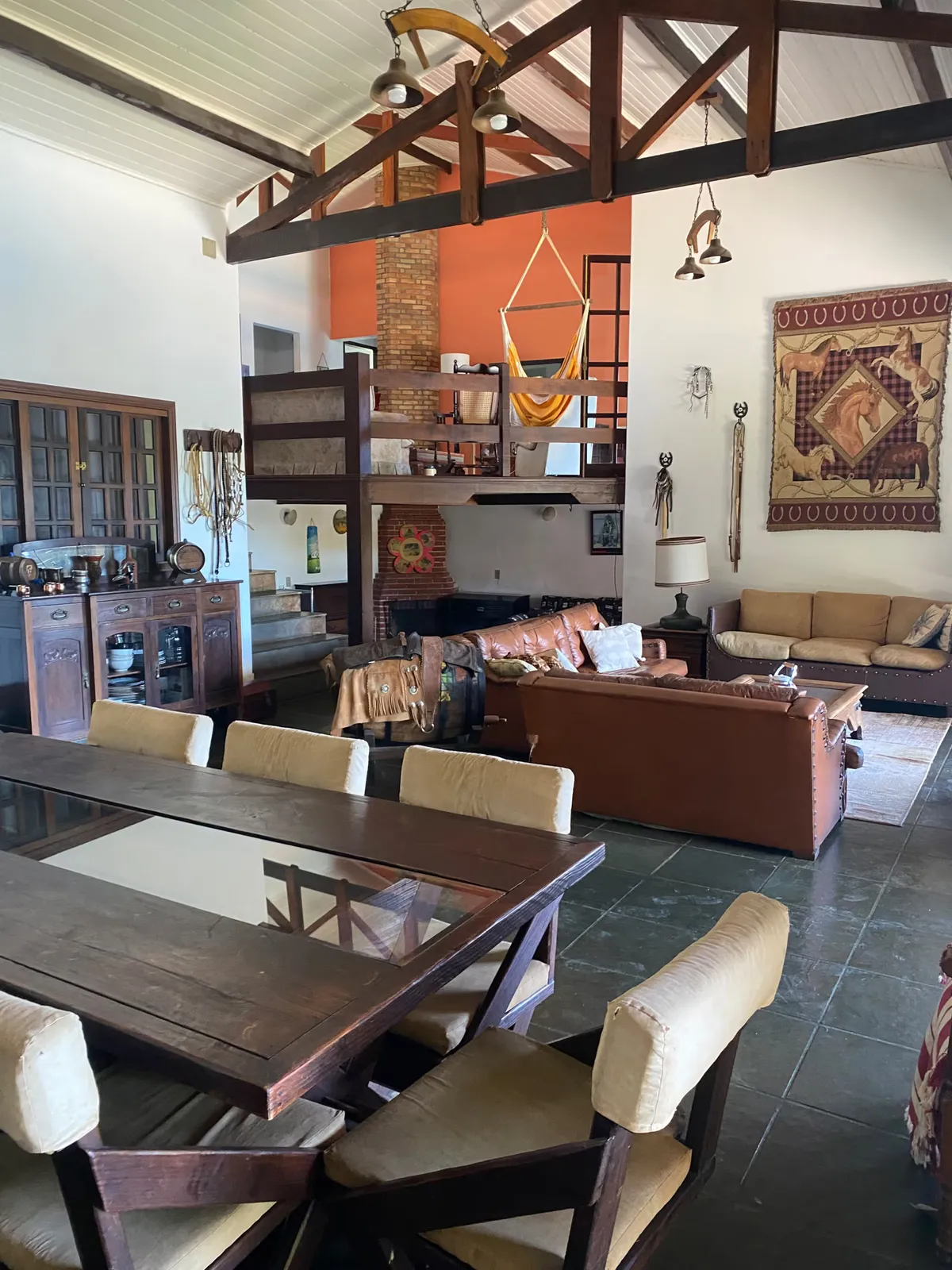 Living da casa sede do Sítio Manacás com mesa de jantar grande, sofás de couro e decoração de fazenda