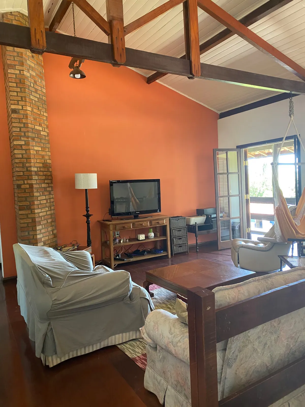 Sala de TV do Sítio Manacás com poltronas, rede suspensa e saída para a varanda