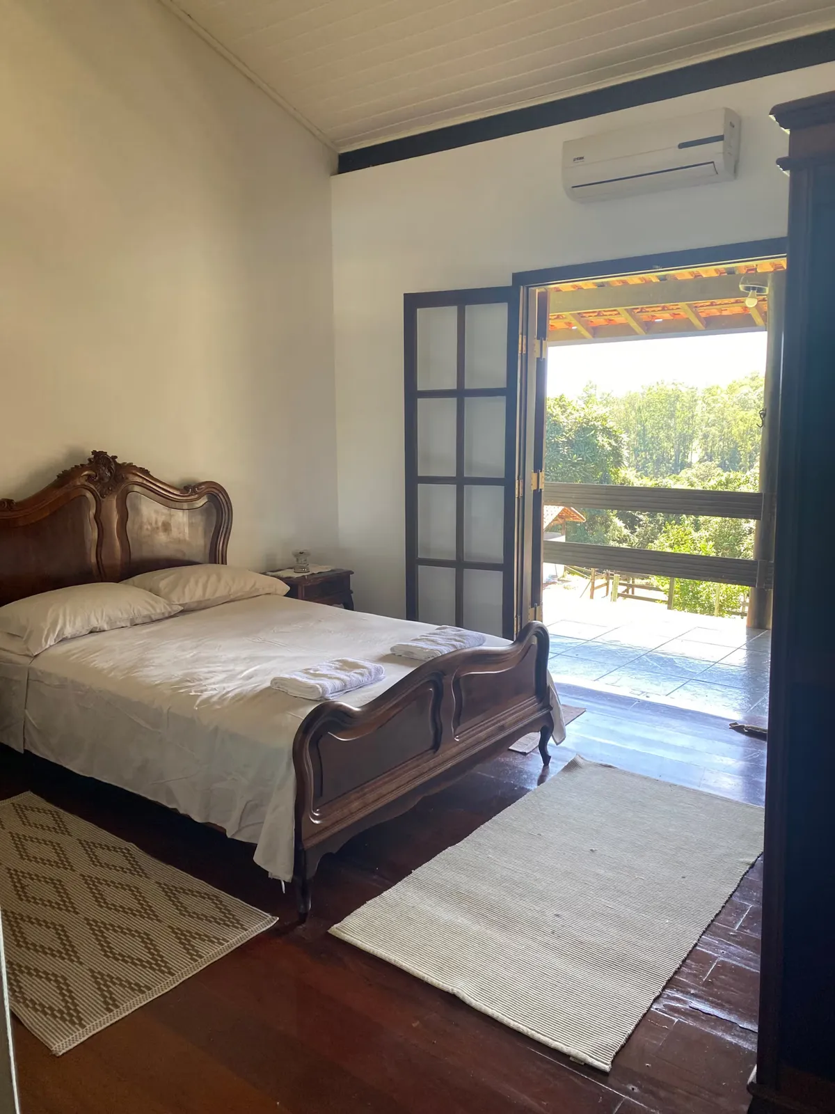 Suíte do casal na casa sede do Sítio Manacás com cama de madeira antiga e portas abertas para a varanda